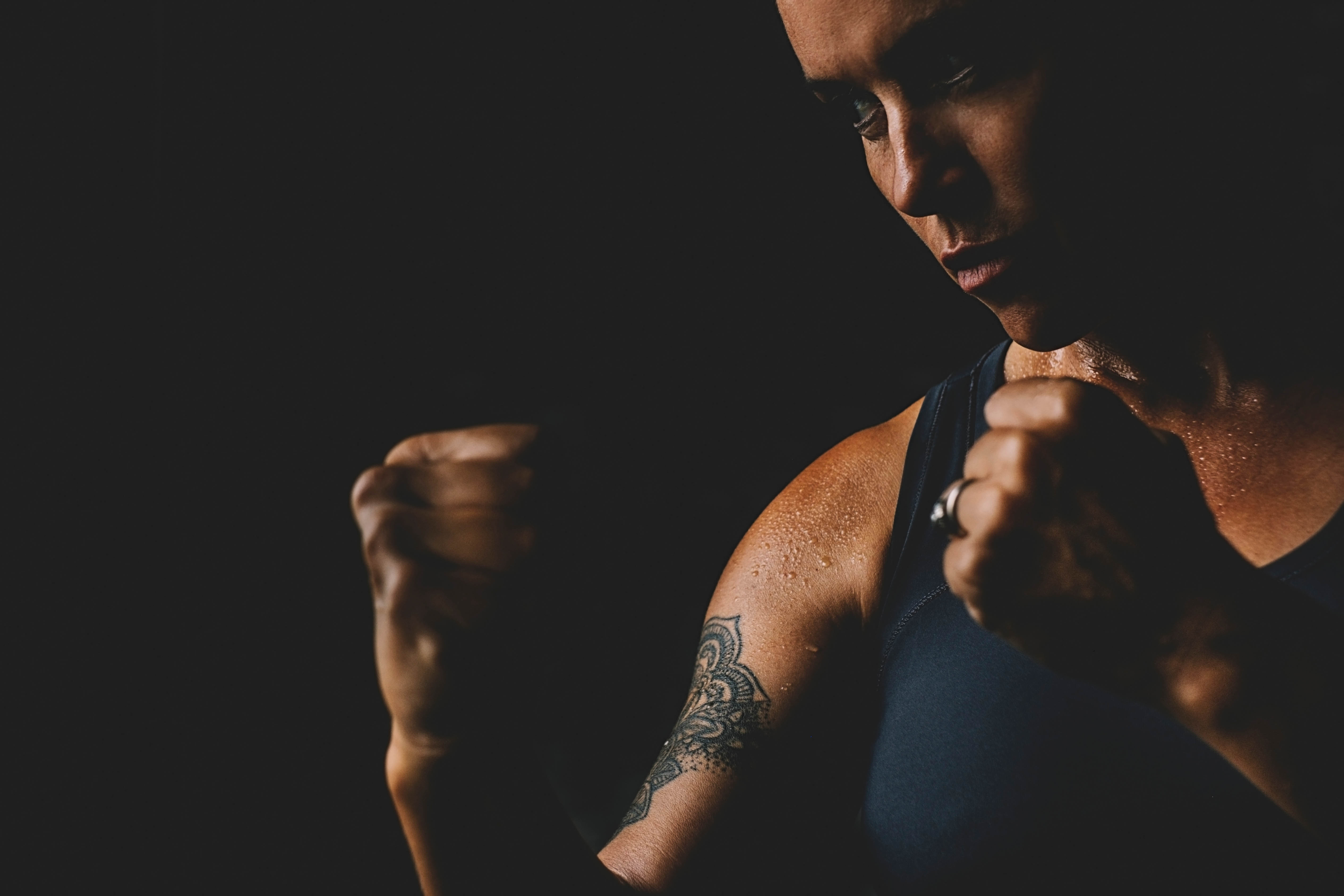 Strong woman boxer with a tattoo, with her fists up in a dark room